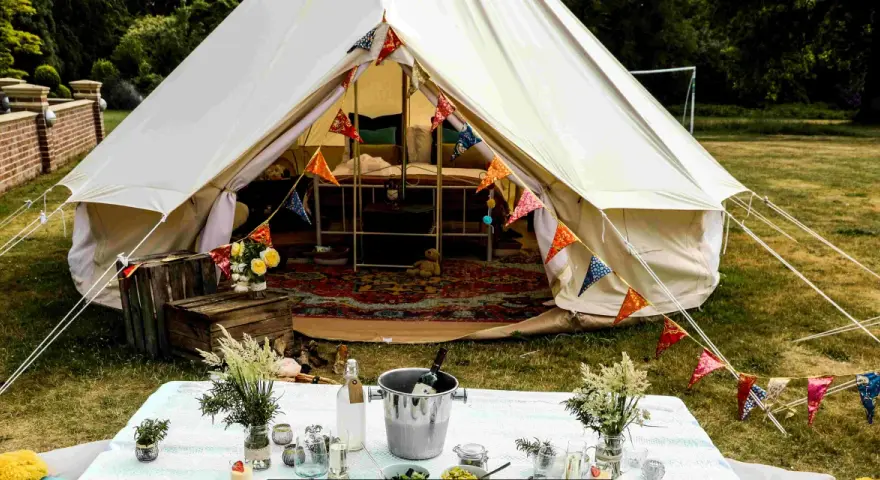 Idealne miejsce na glamping: namiot typu bell z kolorowymi chorągiewkami, stół z winem i kwiatami.
