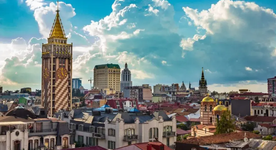 Widok na stolicę Adżarii, Batumi, z charakterystyczną wieżą zegarową i złotymi kopułami cerkwi pod błękitnym, chmurowym niebem.