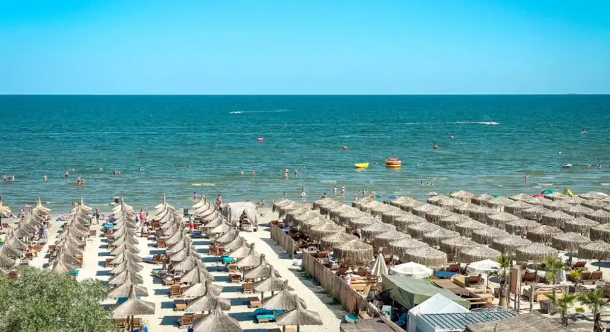 Słoneczna plaża w Rumunii, pełna leżaków i parasoli. Ludzie kąpią się w morzu, idealne miejsce na wakacje.