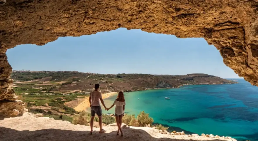 Para zakochanych podziwia widok na turkusowe morze i plażę z jaskini. Malta w styczniu pogoda idealna na spacer.