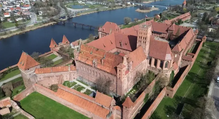Potężny zamek z czerwonej cegły, największy zamek w Europie, otoczony murami obronnymi, nad rzeką.