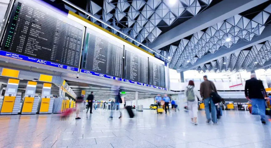 Lotnisko, tablica odlotów, ludzie z bagażami. "Boarding co to?" - to informacja o wejściu na pokład samolotu.