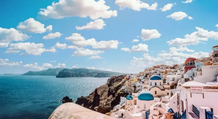 Santorini, Grecja. Białe domy z niebieskimi kopułami na klifie nad morzem. Zastanawiasz się, ile się leci do Grecji?