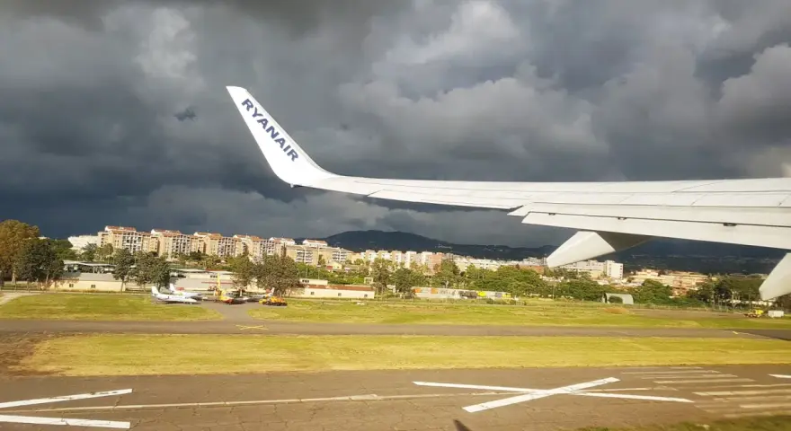 Skrzydło samolotu Ryanair nad lotniskiem, ciemne chmury na niebie.