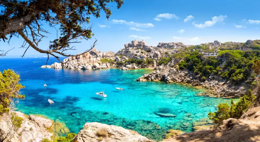 Turkusowa zatoka Costa Smeralda z łodziami i skalistym wybrzeżem.