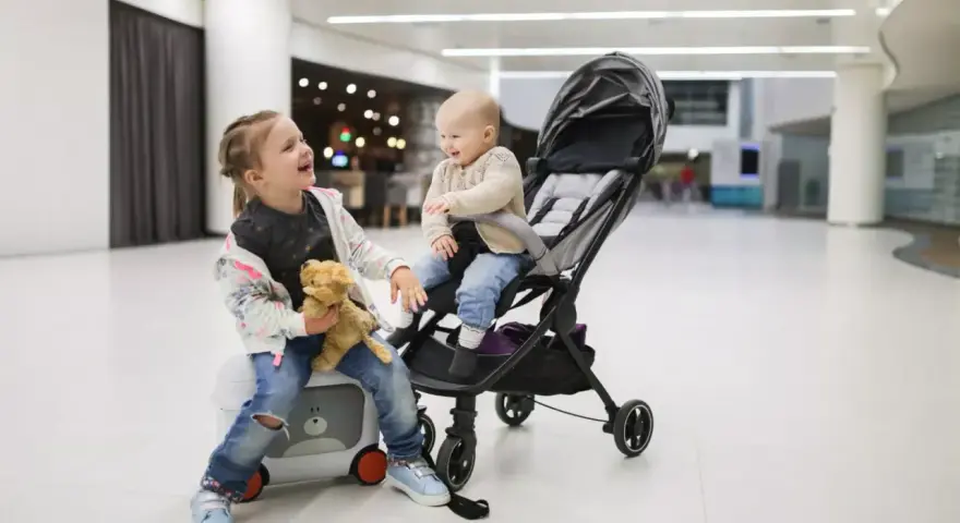 Dzieci w podróży z Ryanair. Starsza siostra siedzi na walizce z misiem, młodsza w wózku.