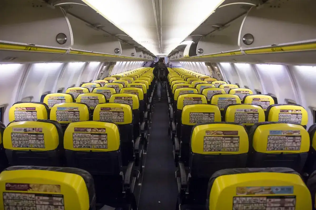 Puste rzędy żółtych siedzeń w samolocie Ryanair. Widać instrukcje bezpieczeństwa na oparciach.