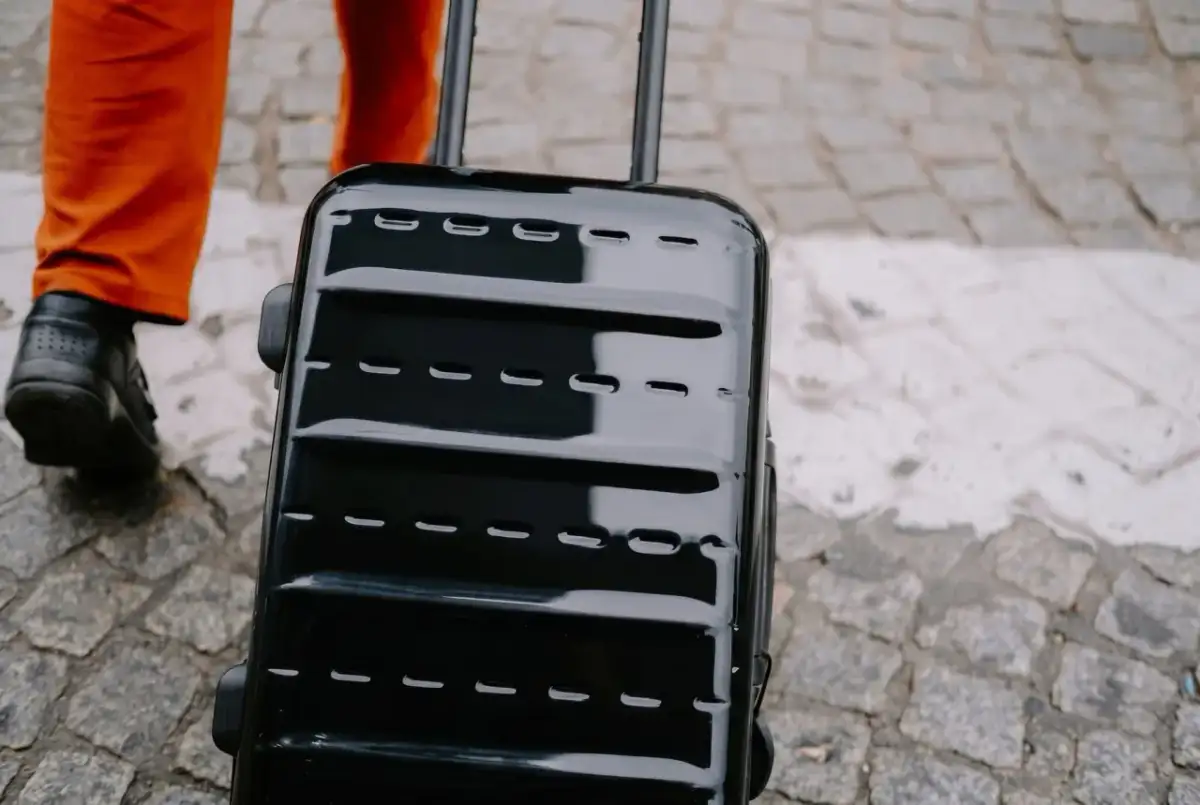 Błyszcząca, czarna walizka, idealna jako bagaż podręczny Ryanair, ciągnięta po bruku.
