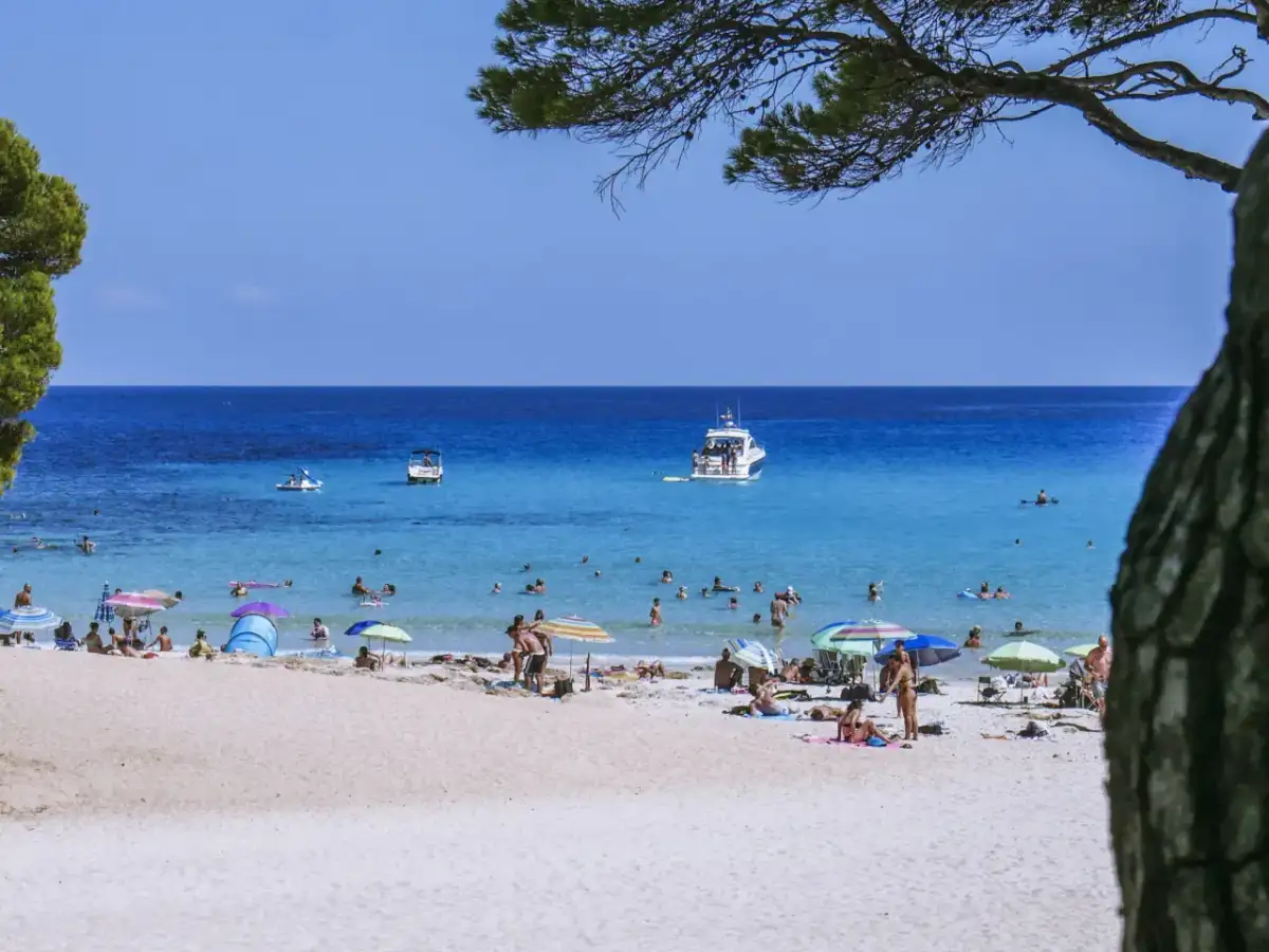 Baleary jakie wyspy? Słoneczna plaża z turkusową wodą, łodziami i ludźmi odpoczywającymi pod parasolami.
