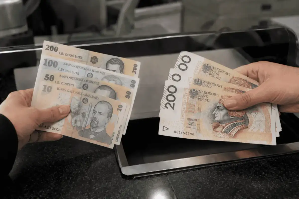 Ręce trzymają banknoty. Jedna ręka pokazuje rumuńską walutę: 10, 50, 100 i 200 lejów. Druga ręka pokazuje polskie banknoty 200 zł.