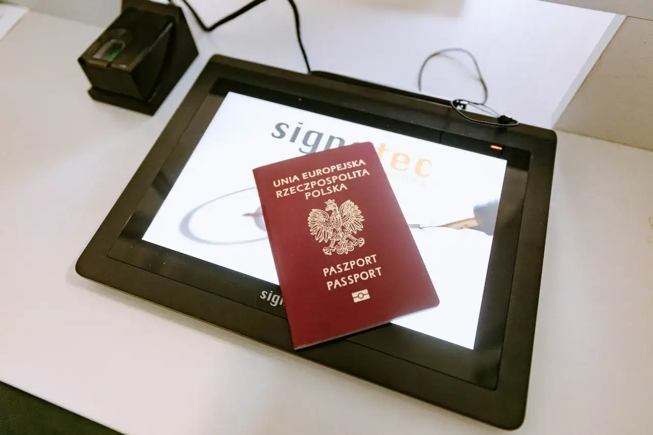 Polski paszport biometryczny leży na ekranie tabletu. Obok widoczny czytnik linii papilarnych.
