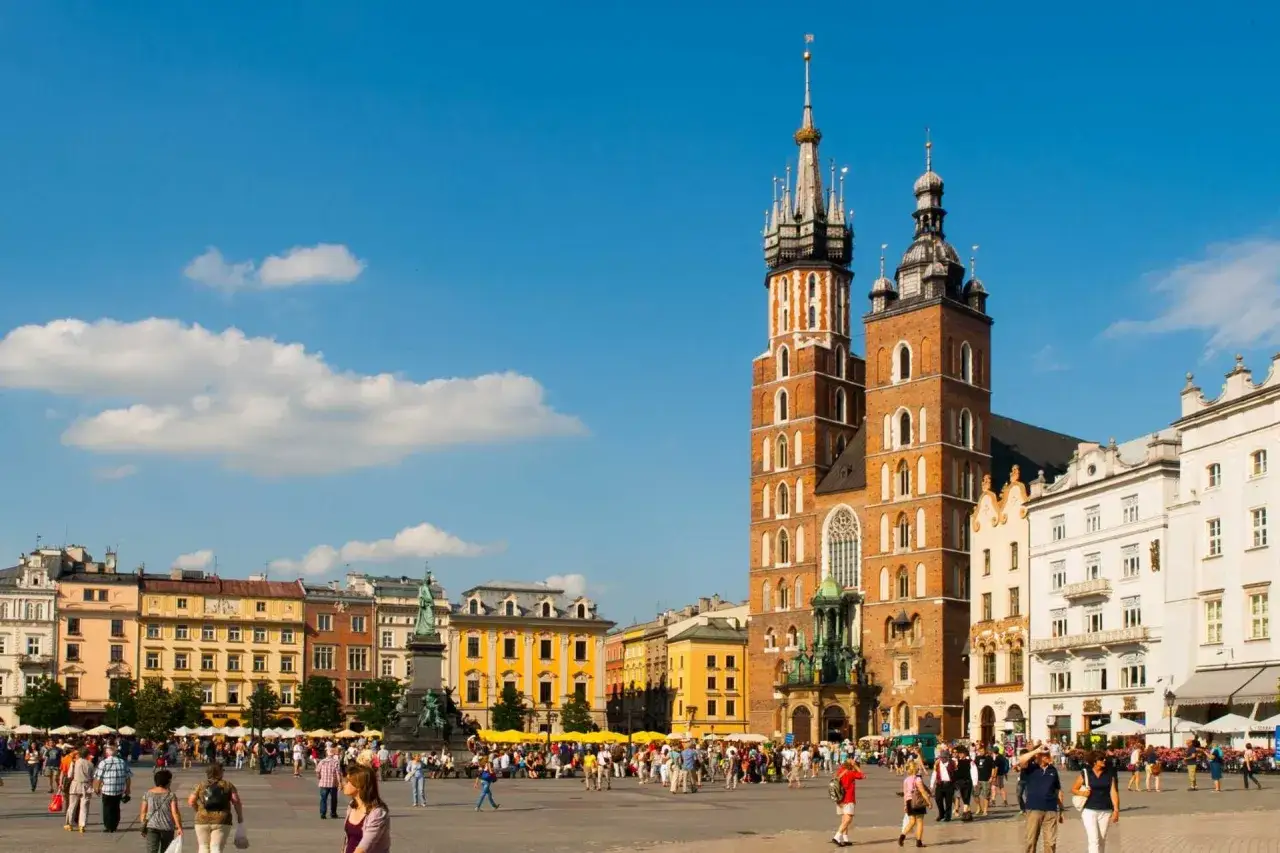 Rynek Główny w Krakowie tętni życiem. W tle Bazylika Mariacka, a wokół kolorowe kamienice. Ciekawostki o Krakowie czekają na odkrycie!