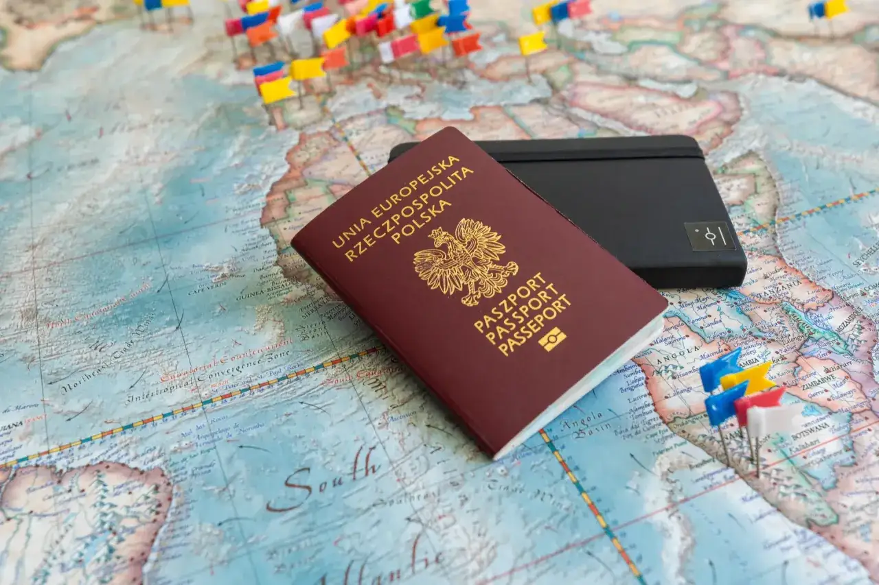 Polski paszport i czarne etui na mapie świata z kolorowymi chorągiewkami. Gotowy na podróż, wniosek o paszport złożony.