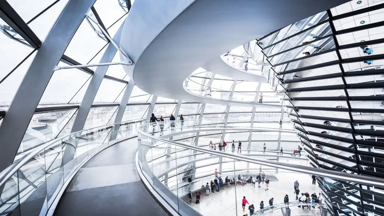 Wnętrze kopuły Reichstagu z krętymi rampami i ludźmi spacerującymi po szklanych balustradach.