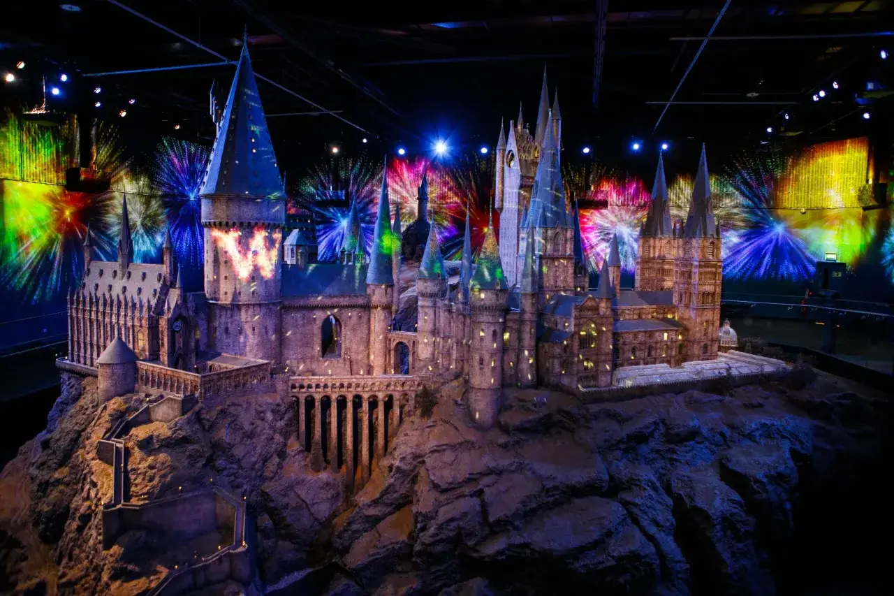 Model zamku Hogwart w muzeum Harry'ego Pottera, oświetlony magicznymi projekcjami przypominającymi fajerwerki.