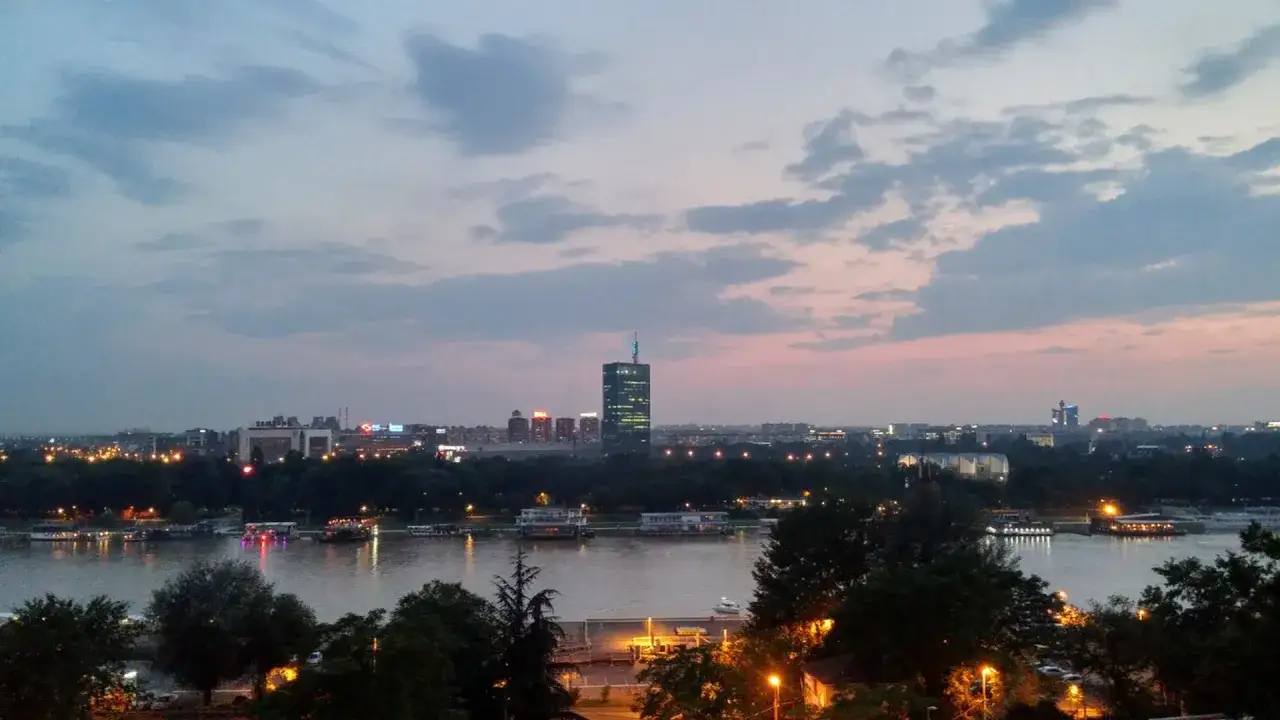Wieczorny widok na Belgrad, stolicę Serbii. Rzeka, łodzie i oświetlone budynki tworzą malowniczy krajobraz.
